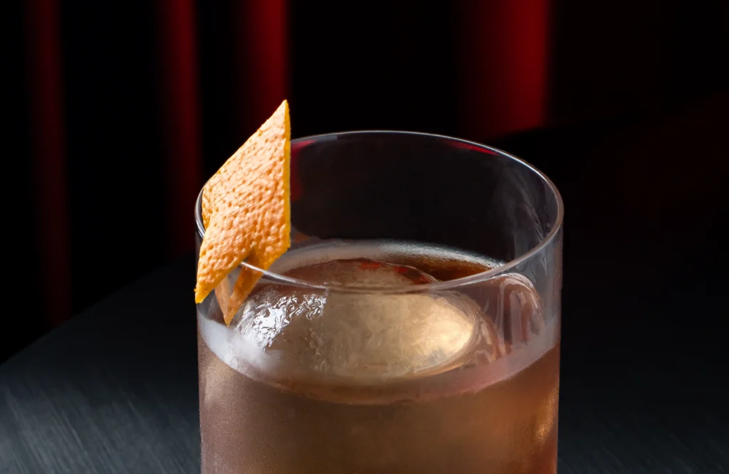 Cóctel Proxy de tequila con Absinth y naranja servido en vaso old fashioned con bloque de hielo y diamante de piel de naranja.