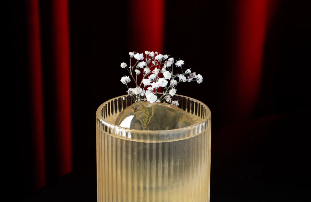 Cóctel G Collins con 1800 Guachimontón servido en vaso highball con hielo y decoración de flores tipo nube.